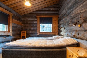Une chambre à coucher située dans une cabane en rondins, avec un lit, une fenêtre, une lampe de chevet et une table de chevet en bois.