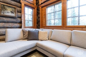 A log cabin interior with a sectional sofa, large windows, and a framed picture on the wall.