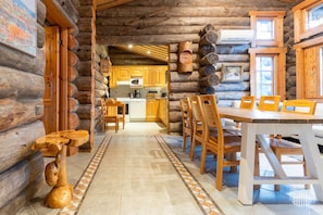 A log cabin interior with a dining area, kitchen, and a view of the outside.