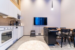 A modern kitchen with a flat-screen TV mounted on the wall, a dining area with a wooden table and chairs, and a small step stool. - Levi West Slope 4 by Holiday in Lapland (Levi)