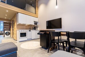 A modern kitchen with white appliances, a dining area with black chairs, and a flat-screen TV mounted on the wall. - Levi West Slope 4 by Holiday in Lapland (Levi)