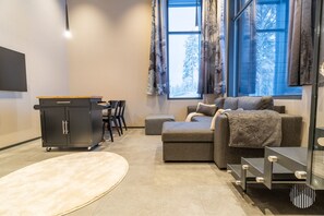 Ein modernes Wohnzimmer mit einer Couch, einem kleinen Tisch, einem Schrank und einem großen Fenster mit Vorhängen.