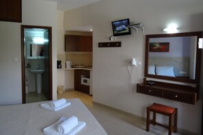 A hotel room with a bed, a small stool, a television, a mirror, and a kitchenette. - Holiday Apartment in Paleochora With a Balcony (Kantanos-Selino)