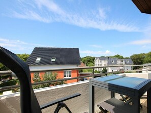 A balcony with a table and chair, overlooking a residential area with houses and trees. - Holiday Apartment With 1 Bedroom (Wyk auf Foehr)