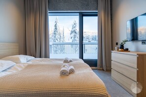 A hotel room with a bed, a dresser, a TV, and a balcony with a snowy view. - Levi West Peak View by Holiday in Lapland (Levi)