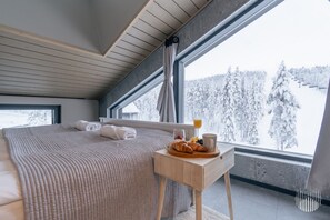 A bedroom with a large bed, a wooden bedside table with breakfast items, and a view of a snowy landscape through a window. - Levi West Peak View by Holiday in Lapland (Levi)