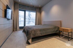 A bedroom with a bed, a nightstand, a window with curtains, and a view of a snowy landscape. - Levi West Peak View by Holiday in Lapland (Levi)