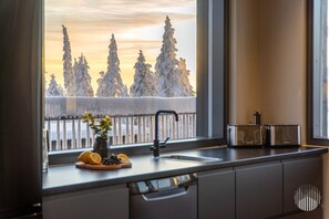 A kitchen with a window view of snow-covered trees and a sunset. - Levi West Peak View by Holiday in Lapland (Levi)