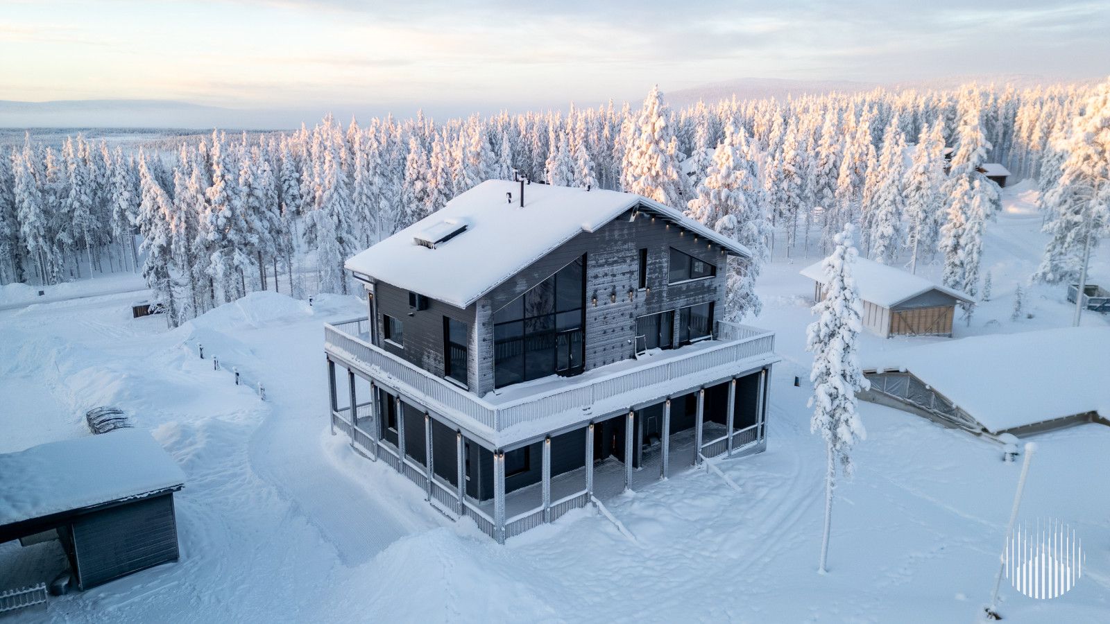 Une cabane moderne à deux étages, dotée d’un balcon et entourée d’une forêt enneigée.