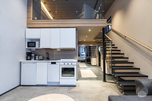 A modern kitchen with white cabinetry, a built-in oven, and a coffee maker. There is a staircase with black railings leading to an upper level. - Levi West Slope 3 by Holiday in Lapland (Levi)