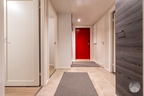 A hallway with a red door at the end, a grey mat at the entrance, and a wooden panel on the right. - Postintie 3 A 6108 by Holiday in Lapland (Levi)