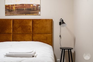 A neatly made bed with white linens and a folded towel, a modern headboard, a wall-mounted lamp, and a small round table. - Postintie 3 A 6108 by Holiday in Lapland (Levi)