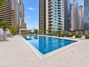 A swimming pool with lounge chairs and a view of tall buildings. - Luxe 1BR with Work Desk and Pool in Dubai Marina (Dubai)