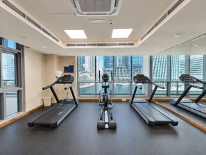 A gym with treadmills, an elliptical, and a rowing machine, large windows, and a view of a cityscape. - Luxe 1BR with Work Desk and Pool in Dubai Marina (Dubai)