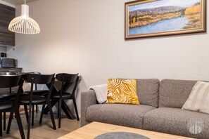 Un salon moderne avec un canapé gris, une table basse en bois et un tableau représentant un paysage.
