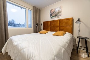 Une chambre d’hôtel avec un grand lit, une tête de lit, une table de chevet, une lampe et une fenêtre donnant sur des arbres.