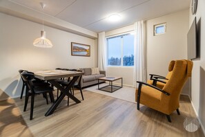 Ein modernes Wohnzimmer mit Esstisch, Sofa und Sessel, einem Fenster mit Blick und einem Gemälde an der Wand.