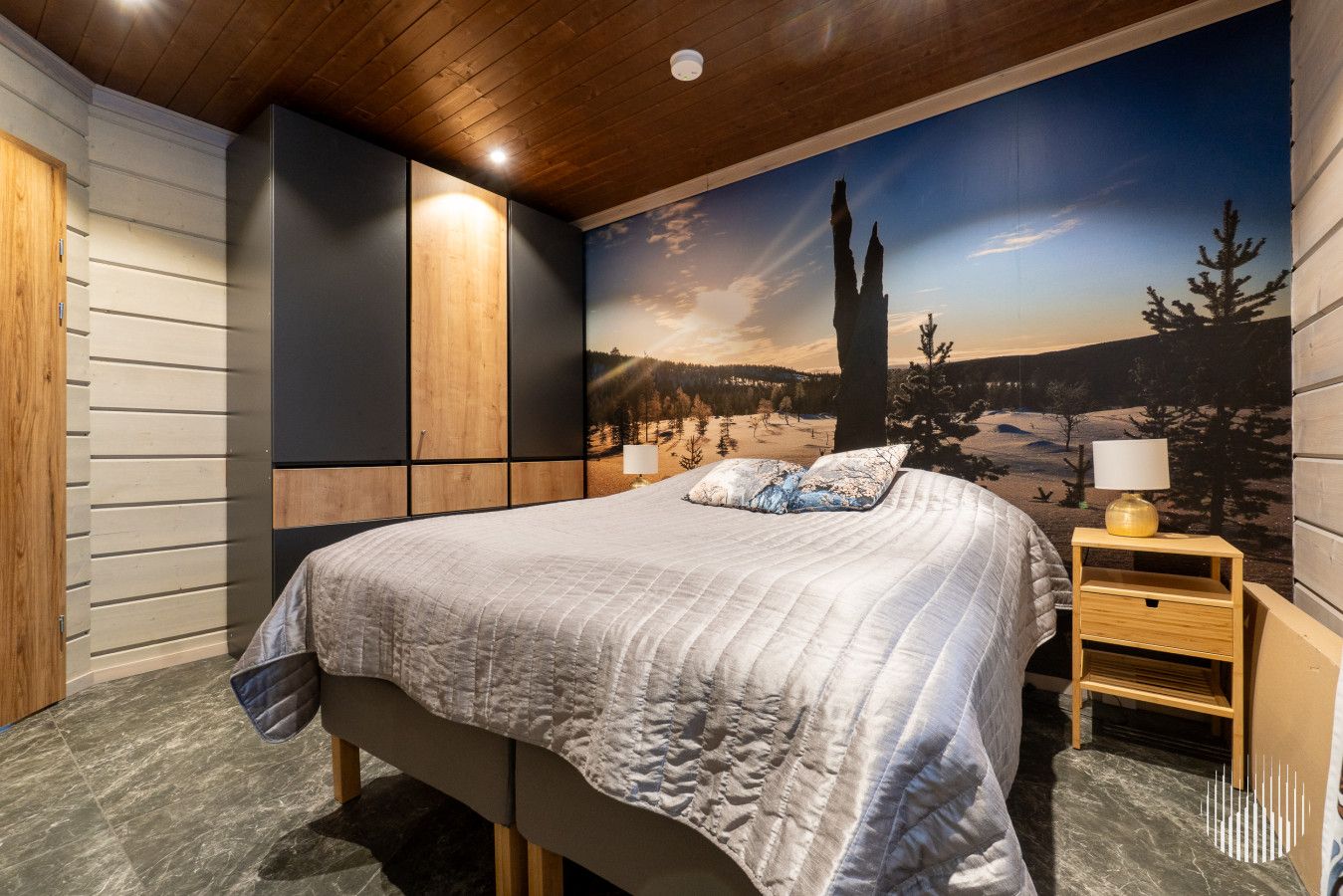 Une chambre à coucher avec un grand lit, une table de chevet, un meuble fixé au mur et une fresque représentant un paysage montagneux.