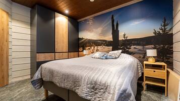 Une chambre à coucher avec un grand lit, une table de chevet, un meuble fixé au mur et une fresque représentant un paysage montagneux.
