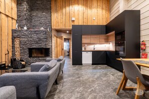 Un interior moderno con chimenea de piedra, sofás grises, una mesa de comedor de madera y una zona de cocina.
