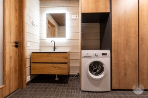 A compact laundry room with a washing machine, wooden cabinets, and a mirror.