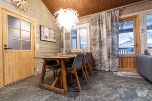 A dining area with a wooden table and chairs, a chandelier, and a view of the outside.