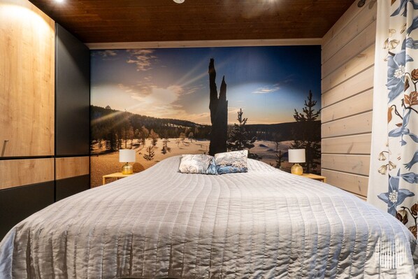 A bedroom with a large bed, two bedside lamps, and a wall mural of a mountainous landscape.
