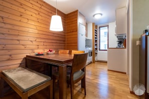 Um quarto com painéis de madeira, uma mesa de jantar e cadeiras, um lustre e uma área de cozinha ao fundo.