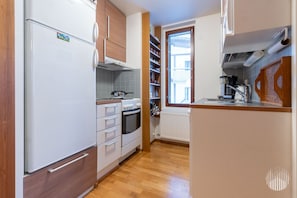 Cocina pequeña con refrigerador, horno y estufa, gabinetes de madera y una ventana con persianas.