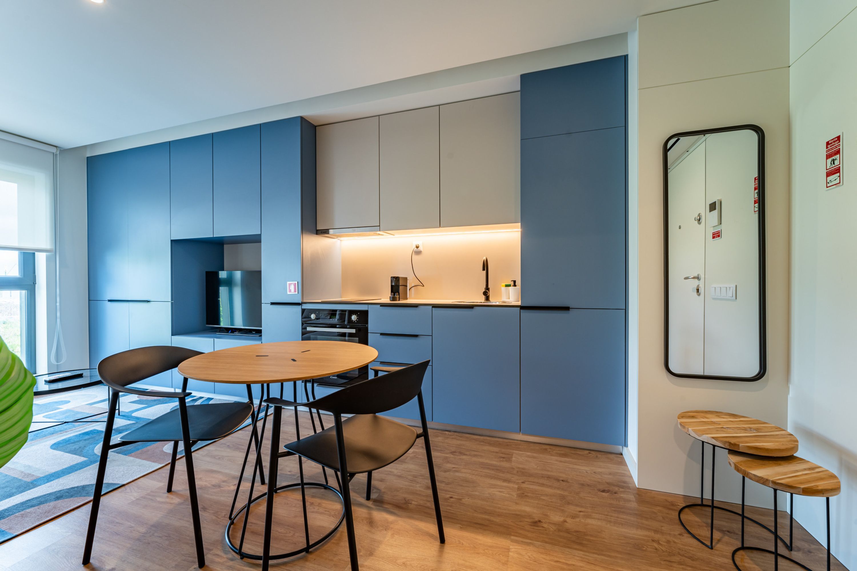 A modern kitchen with blue cabinets, a round wooden table, and black chairs.