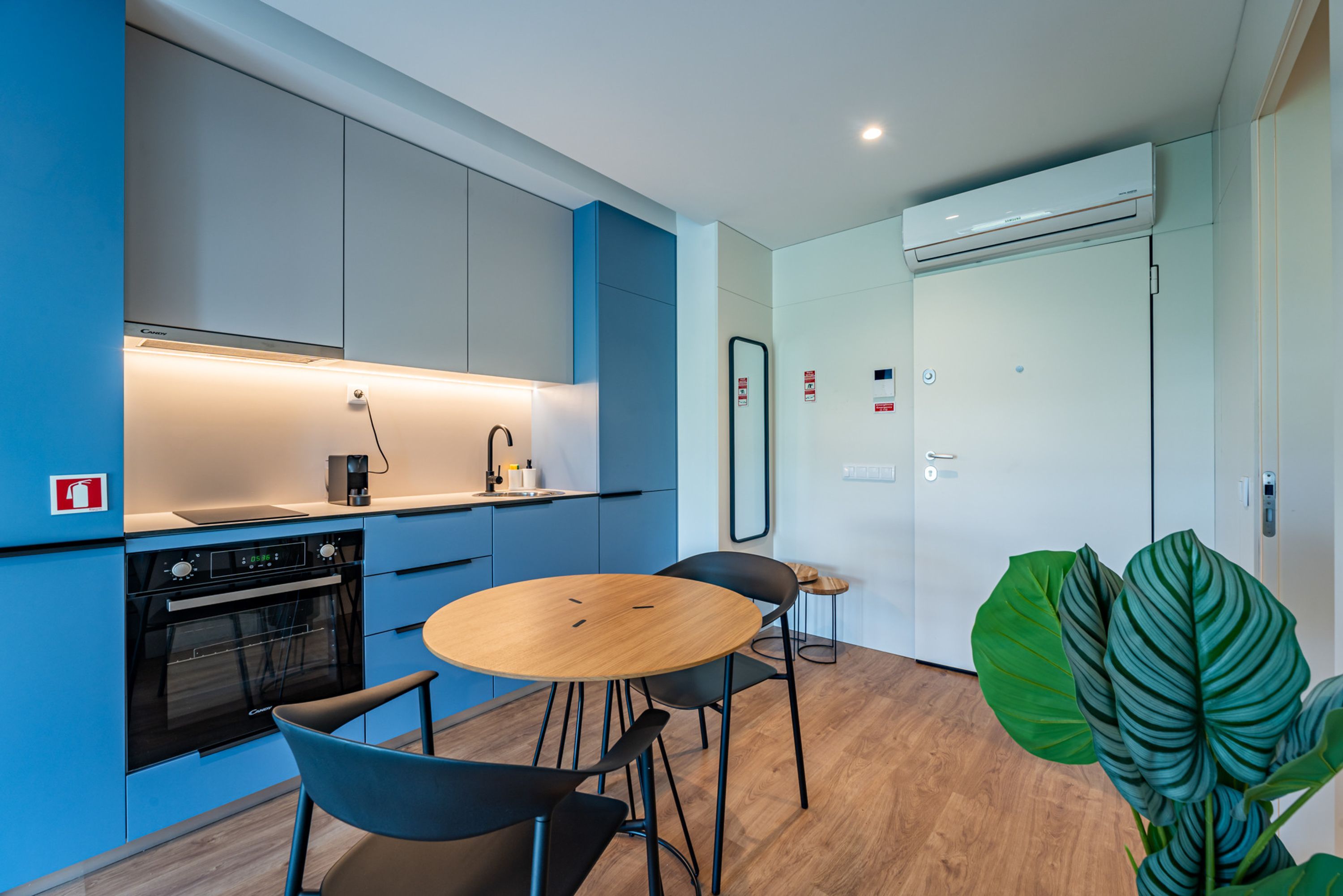 Una cocina moderna con horno empotrado, cafetera y lavabo. Hay un comedor con una mesa redonda de madera y dos sillas.