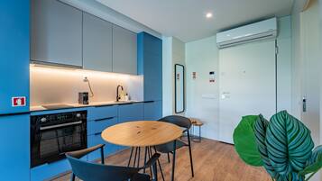 A modern kitchen with a built-in oven, a coffee machine, and a sink. There is a dining area with a round wooden table and two chairs.