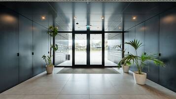 A modern building entrance with a glass door, potted plants, and a tiled floor.
