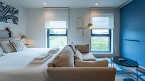Ein modernes Schlafzimmer mit einem großen Bett, einer Couch, einem kleinen Tisch und zwei Fenstern mit Blick.