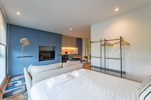 Habitació d'hotel moderna amb llit, televisió, escriptori i petita cuina.