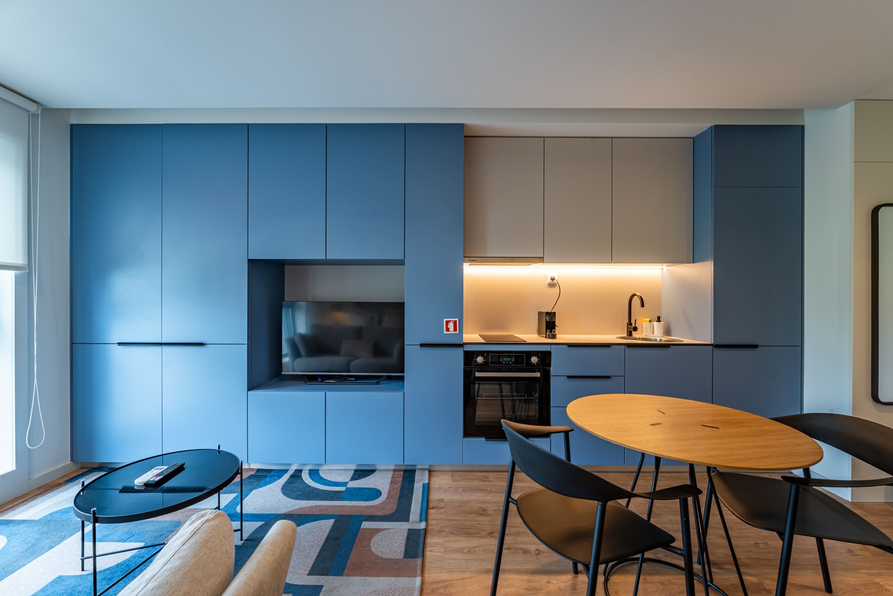 Una cocina moderna con armarios azules, horno empotrado y comedor con mesa y sillas redondas.