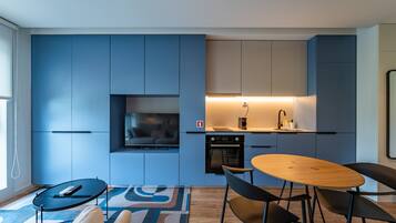 A modern kitchen with blue cabinetry, a built-in oven, and a dining area with a round table and chairs.