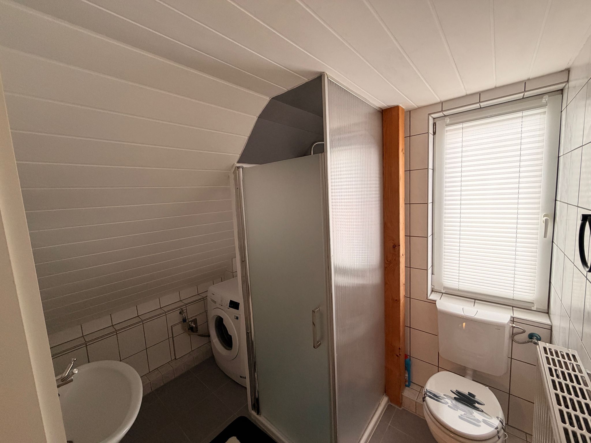 Ein kleines Badezimmer mit Dusche, Toilette und Waschmaschine.