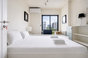 Ein Hotelzimmer mit Bett, Schreibtisch, Stuhl, Fenster mit Blick auf Gebäude und Heizkörper.