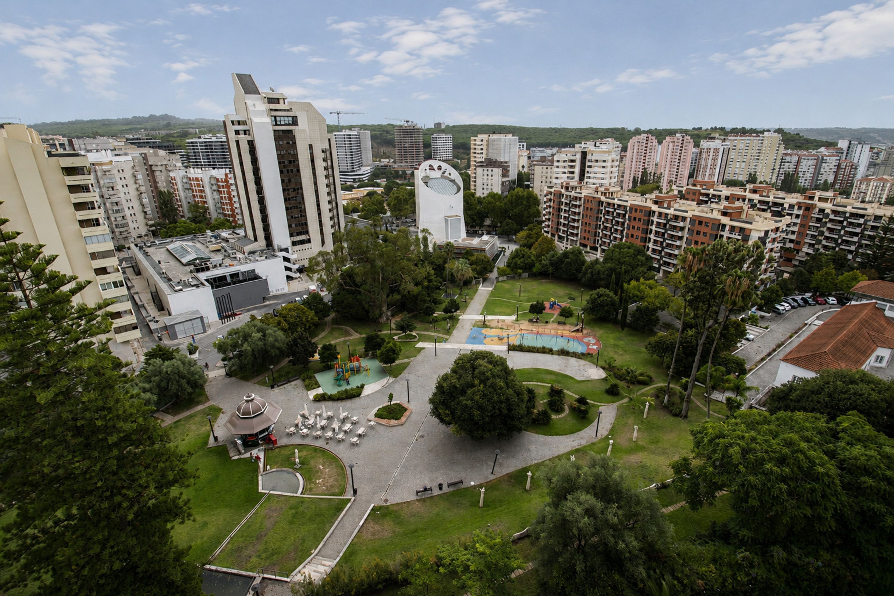 Um edifício alto com design arquitetônico único, rodeado por um parque com parquinhos e áreas de estar.