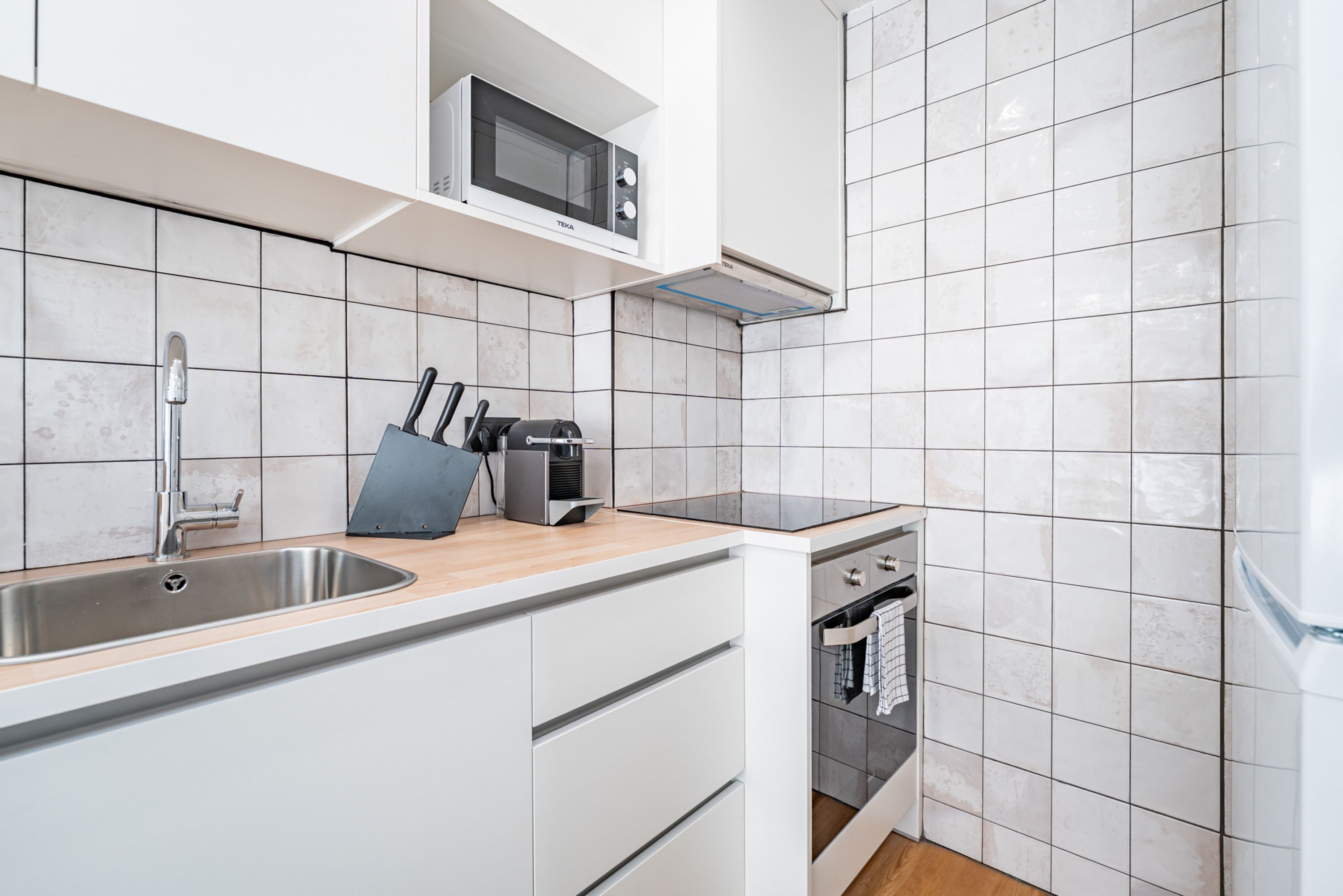 Una cocina moderna con armarios blancos, un lavamanos de acero inoxidable, un microondas y un horno empotrado.
