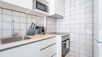 Una cocina moderna con armarios blancos, un lavamanos de acero inoxidable, un microondas y un horno empotrado.