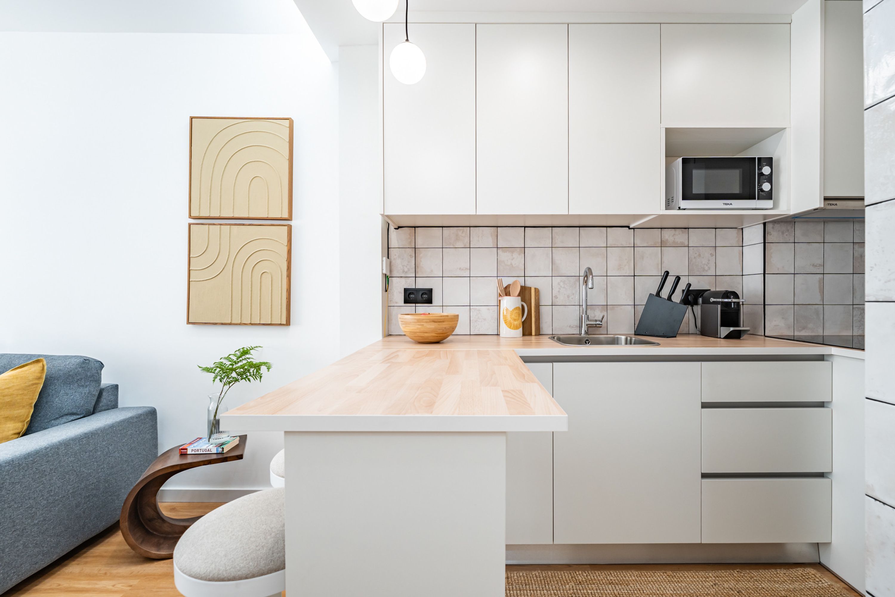 Una cocina moderna con armarios blancos, encimera de madera y microondas integrado.