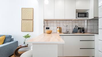 Una cocina moderna con armarios blancos, encimera de madera y microondas integrado.
