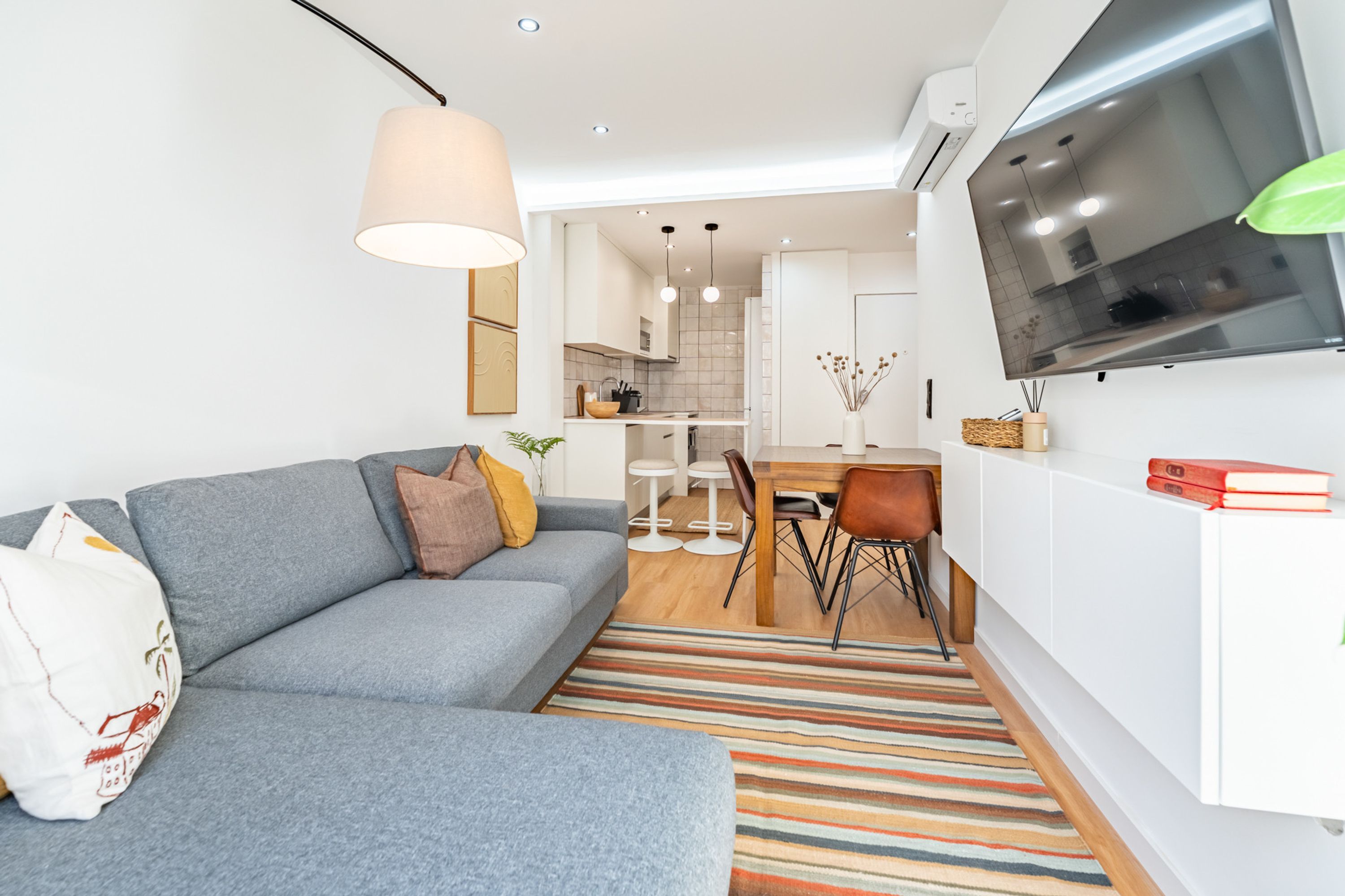 Una sala de estar moderna con un sofá gris, un tapete a rayas y un comedor con mesa y sillas blancas.