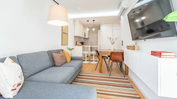 Una sala de estar moderna con un sofá gris, un tapete a rayas y un comedor con mesa y sillas blancas.