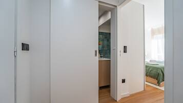 Habitación de hotel con piso de madera, cubrecama verde y baño con pared de azulejos y lavamanos.