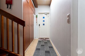 Un couloir étroit, avec une rambarde en bois d’un côté, un tapis à motifs sur le sol et une porte blanche au fond.