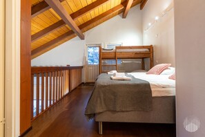 Une chambre avec un lit superposé, des poutres en bois, une fenêtre et une vue sur l’extérieur.