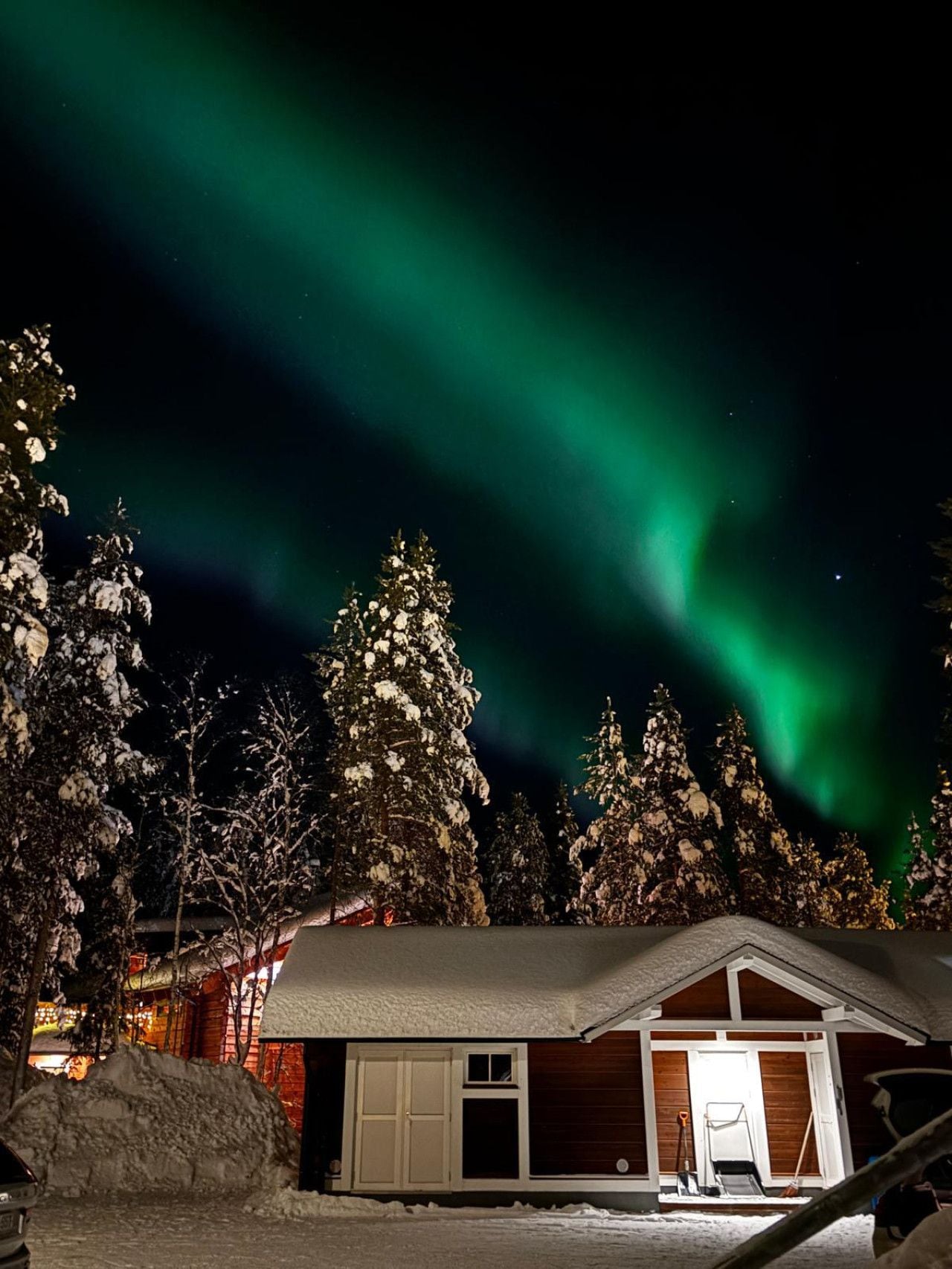 A cabin with a snow-covered roof, a garage, and a view of the northern lights.